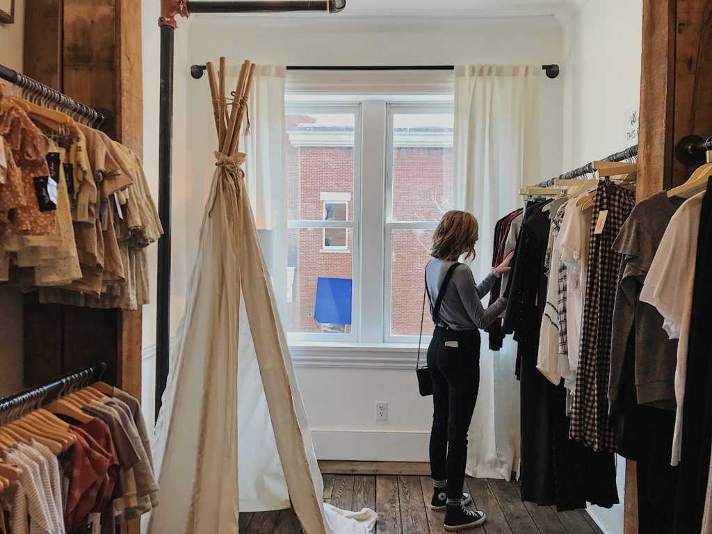Woman browsing a clothes rack inside a retail store.
