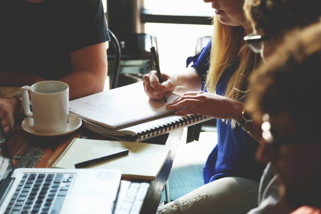 An image of a woman writing in a notebook during a meeting.