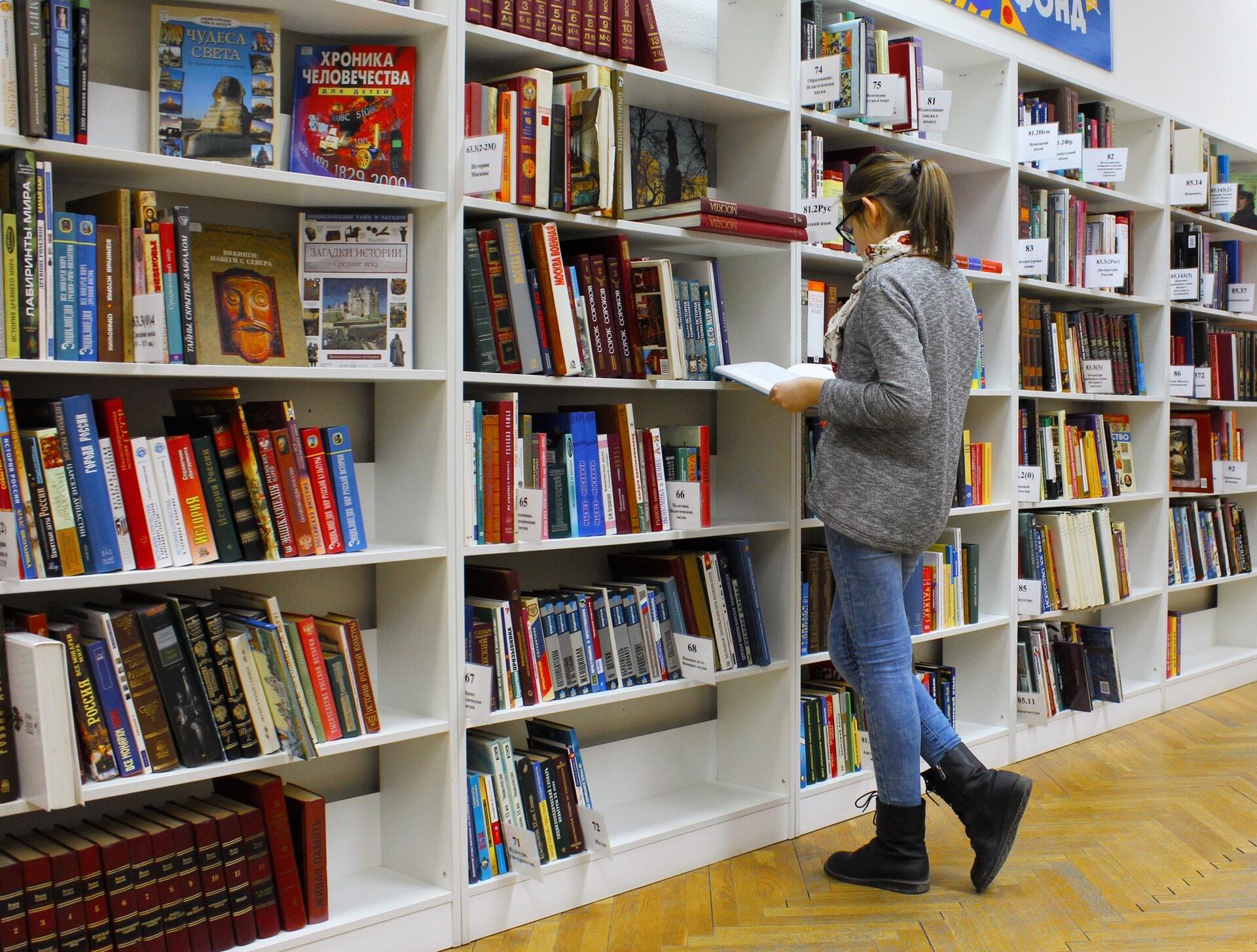 An image of woman looking at a book in front of bookshelves in a store.